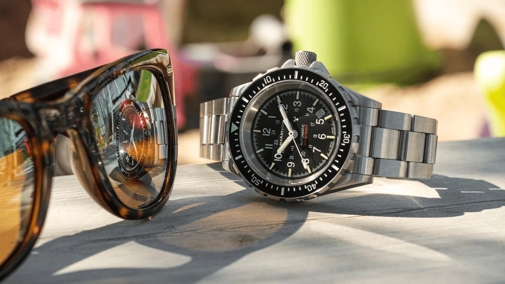 Watch and sunglasses on a reflective surface with blurred background