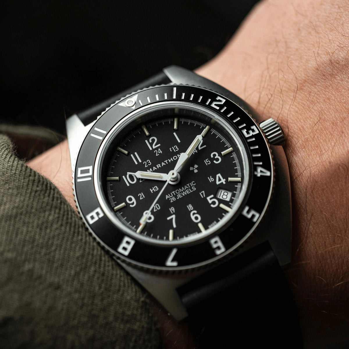 Black wristwatch with a detailed face on a person's wrist against a dark background