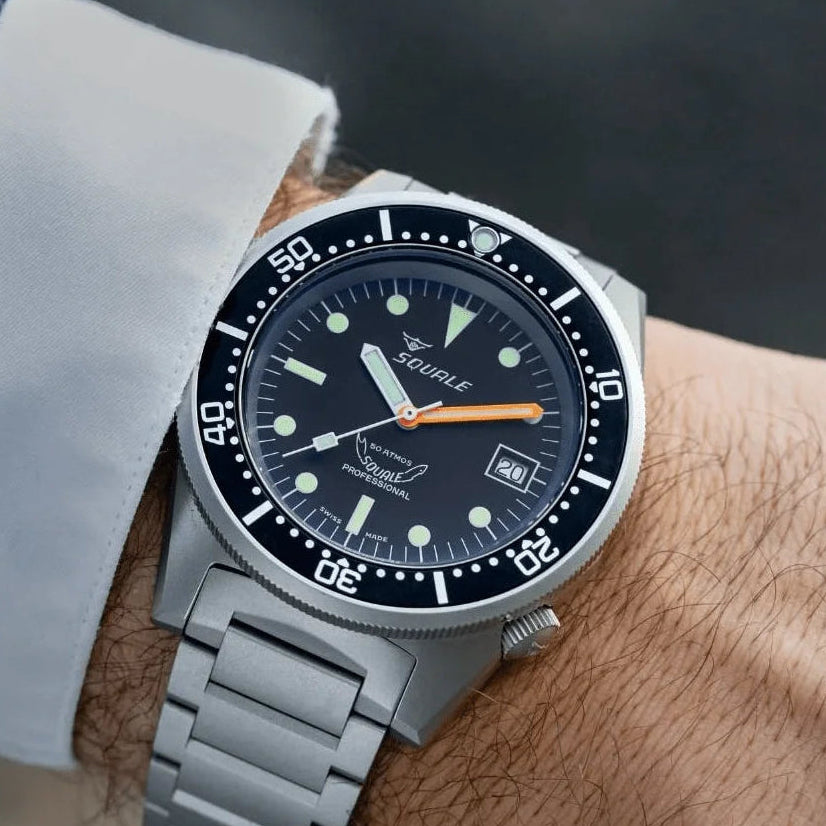 Silver watch with a black dial on a person's wrist against a blurred background